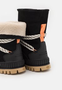 Bottes d'hiver noires et beiges avec un doux bord en fourrure, des accents orange contrastants, des lacets épais et des semelles en caoutchouc texturé.