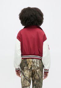 Κόκκινο και λευκό μπουφάν τύπου bomber με ριμπ τελείωμα και μανσέτες, που διαθέτει ψηλό γιακά και υπερμεγέθη μανίκια, σε συνδυασμό με παντελόνι καμουφλάζ.