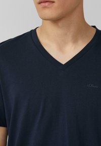 Granatowa koszulka V-neck z krótkim rękawem, wykonana z miękkiego materiału; na lewej piersi znajduje się małe logo s.Oliver. Gładka tekstura i swobodny krój.