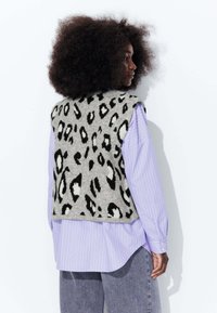 Gilet en laine gris avec un imprimé léopard noir et blanc, doté d'un col rond et d'un design sans manches, porté par-dessus une chemise rayée lavande.