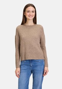 Lichtbruine wollen trui met een ribgebreide zoom en manchetten, voorzien van een ronde hals en licht verlaagde schouders, gecombineerd met blauwe jeans.