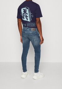 Camiseta navy con estampado gráfico en la parte posterior, combinada con jeans de corte slim de lavados medios y zapatillas blancas. Tejido texturizado, diseño informal.