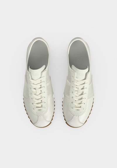 Paire de baskets en cuir blanc avec lacets et semelles marron rainurées vue de dessus sur fond blanc.