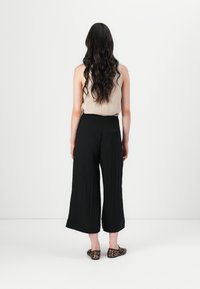 Pantaloni neri a gamba larga con texture plissettata, vita alta e due tasche posteriori, abbinati a un top beige e scarpe ballerine con stampa leopardata.