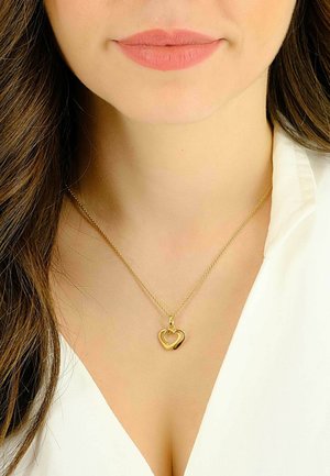 Collana con pendente a forma di cuore in oro su una delicata catena, con un design a doppio cuore, posata su una camicia bianca.