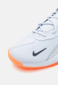 Light blue athletic shoe featuring a textured upper, black swoosh logo, and an orange rubber sole with a patterned accent.