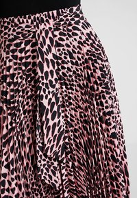 Plisovaná sukně v růžové látce s černým zvířecím vzorem, se širokým pasem a uvázaným detailem na přední straně.