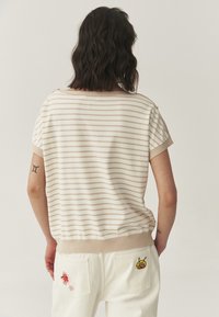 Haut à manches courtes rayé crème et tan avec un col rond, associé à un pantalon blanc avec des broderies florales et de dessins animés sur les poches.