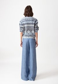 Zils adīts džemperis ar rakstu akcentiem, apvienots ar gaismas zila auduma platām biksēm. Džemperim ir sarullēti piedurkņu gali un ribota apakšmaliņa.