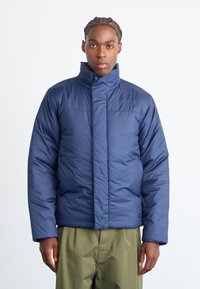Navy blue puffer jacket with high collar, zipper closure, and stitched detailing. Features a logo on the chest and elastic cuffs.