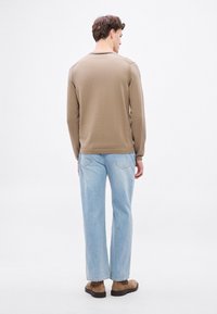 Długa koszula z teksturowanymi plecami, w połączeniu z jasnoniebieskimi prostymi dżinsami i brązowymi butami. Neutralny, luźny krój.