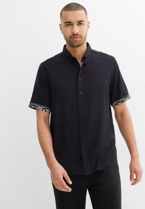 Schwarzes Kurzarmhemd aus glattem Stoff, mit gemusterten Manschetten und einem Button-Down-Kragen. Schlichter vorderer Teil mit funktionalen Knöpfen.