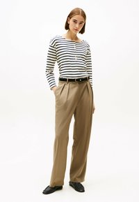 Maglietta a maniche lunghe a righe blu e bianca con bottoni; abbinata a pantaloni beige a vita alta e scarpe nere.