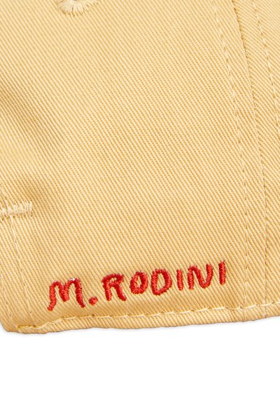 Beige fabric cap with a textured surface, featuring red embroidered text "M. RODINI" on the side. Clean stitching and structured shape.