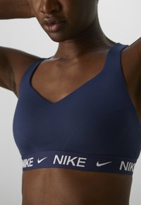 Sutien sport navy cu bretele groase și un design în formă de V. Prezintă un logo alb Nike pe banda elastică pentru un plus de detaliu de branding.