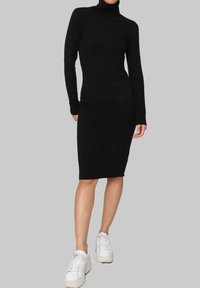 Robe noire en tricot côtelé avec un col roulé haut, des manches longues et une silhouette ajustée, associée à des baskets blanches à semelle épaisse.