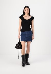 Svart ribbet topp med volangkant, blå denim mini-skjørt, svarte knelang støvletter med spenner, og en svart blomstret snortaske.