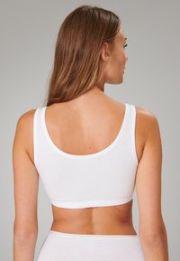 Bralette en coton blanc avec une bande large et lisse et de larges bretelles ; présente un dos en forme de scoop. Texture douce et style minimaliste.