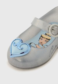 Kimalteleva harmaa Mary Jane -kenkä, jossa on sininen sydänkoriste ja Tuhkimo-kuvake pohjallisessa. Kenkässä on hihna, jossa on pyöreä solki.