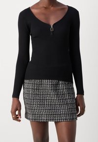 Top lungo a maniche nere a coste con scollatura a V e chiusura con zip, abbinato a una mini gonna in tweed bianco e nero con texture.