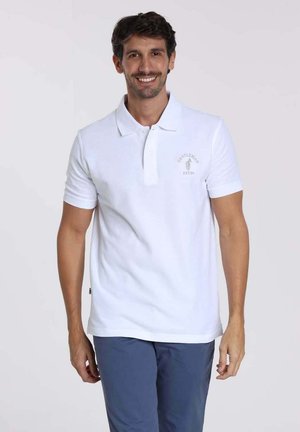 Polo shirt blanc avec un col classique et des manches courtes, arborant un petit logo sur la poitrine. Tissu en coton lisse, coupe régulière.