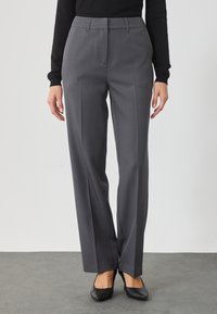 Pantaloni gri, croiți pe măsură, cu un design drept, având dungi subtile, buzunare frontale și o textură netedă. Asortați cu tocuri negre.