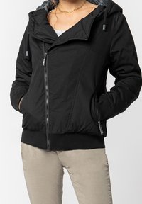 Czarna kurtka na zamek błyskawiczny z kapturem, o gładkiej fakturze, ze ściągaczami na mankietach i dwoma przednimi kieszeniami. Wnętrze wyściełane jest jaśniejszą podszewką.