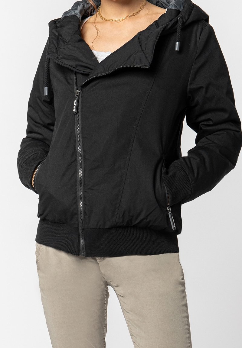 Czarna kurtka na zamek błyskawiczny z kapturem, o gładkiej fakturze, ze ściągaczami na mankietach i dwoma przednimi kieszeniami. Wnętrze wyściełane jest jaśniejszą podszewką.