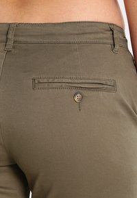 Pantaloni verde oliva con una texture liscia, una tasca posteriore con flap orizzontale e bottone, e passanti per cintura in vita.