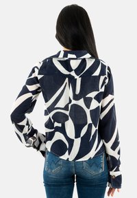 Camisa de manga larga en azul marino y blanco con un collar, que presenta un diseño abstracto y detalles de puños abotonados, fabricada con tejido ligero.