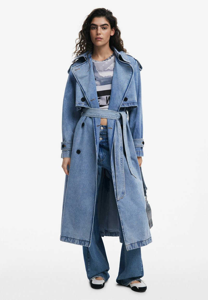 Denim-Trenchcoat in Hellblau, langes Design mit tailliertem Gürtel, ausgestattet mit doppelreihiger Knopfleiste und breiten Revers. Kombiniert mit passenden Jeans.