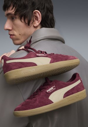 Baskets en daim bordeaux avec des accents crème, semelle en caoutchouc et logo PUMA ; elles présentent une pointe arrondie, un design à lacets et une surface texturée.