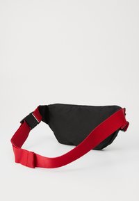 Sort stof bæltetaske med en buet form, der har en bred rød rem og en sort spænde. Holdbart materiale med en struktureret overflade.