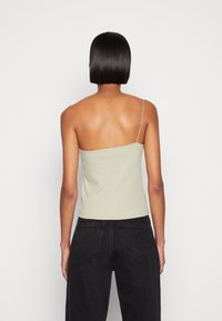 Top a costine verde chiaro con una spalla sottile, abbinato a jeans neri a vita alta, che mostrano una texture liscia e un design semplice.