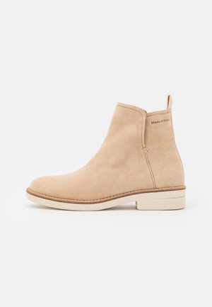 Botín beige de ante con tacón bajo, lengüeta para tirar y detalle de suela cosida, con la marca "Marc O’Polo" cerca del tobillo.