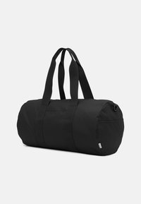 Black duffel bag made of durable fabric, cylindrical shape, features sturdy black straps, zip closure, and a small branded tag.