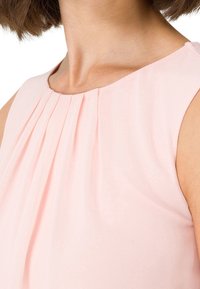 Top sin mangas de color rosa claro con un diseño plisado, textura de tela suave y un escote redondeado. Sin herrajes ni patrones visibles.