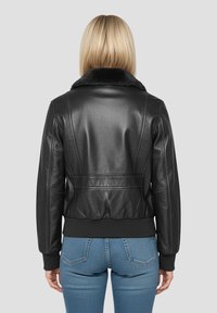 Giacca nera in pelle con colletto in morbida pelliccia nera, polsini a coste e design aderente, che mostra una texture liscia e cuciture dettagliate.