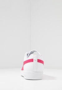 Białe sneakersy z różowym paskiem i logo Puma na pięcie, widok od tyłu, na jednolitym białym tle.