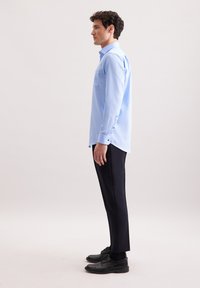 Jasnoniebieska koszula z długim rękawem z kieszonką, z kontrastowymi czarnymi guzikami, połączona z ciemnymi, dopasowanymi spodniami i czarnymi eleganckimi butami.