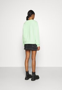 Felpa verde menta con maniche a polsino, abbinata a una gonna di jeans nera. Stivaletti neri con suola spessa. Sfondo neutro.