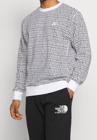 Svart och vit mönstrad sweatshirt med rund halsringning och ribbade ärmslut, i kombination med svarta sweatpants med en vit logotyp.