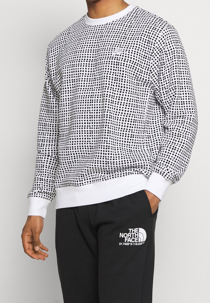 Svart och vit mönstrad sweatshirt med rund halsringning och ribbade ärmslut, i kombination med svarta sweatpants med en vit logotyp.