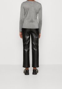 Maglione grigio a maniche lunghe con un effetto metallico, abbinato a pantaloni in pelle neri a vita alta. Texture liscia, design a gamba dritta, dettagli minimal.