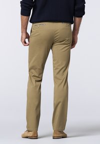 Khaki bukser med slim fit, der har to baglommer med knaplukninger og en glat tekstur. Båret med brune ruskindsko.