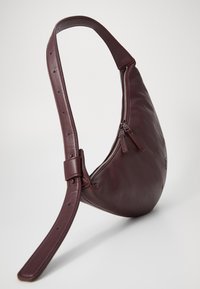 Μπορντό δερμάτινη τσάντα χιαστί με καμπύλη μορφή, ρυθμιζόμενο λουρί και τσέπη με φερμουάρ που διαθέτει δύο φερμουάρ. Λείο υφασμά.