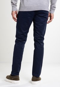 Námořnické modré kalhoty ze směsi bavlny se slim fit střihem, s hladkou texturou a minimálním zdobením, doplněné hnědými semišovými teniskami.