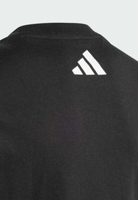 Černé bavlněné tričko s kulatým výstřihem a bílým akcentem tří pruhů na zadní straně blízko límce. Měkká, hladká textura.
