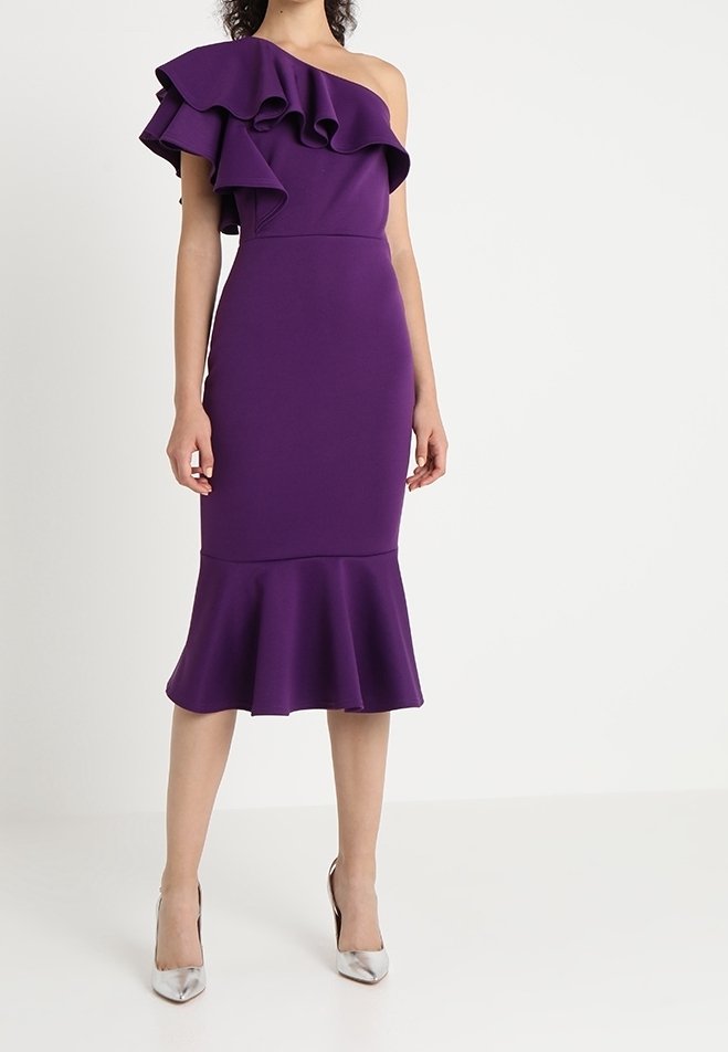 Robe violette ajustée avec une épaule dénudée et des accents à volants. Tissu texturé et ourlet évasé. Associée à des escarpins argentés.