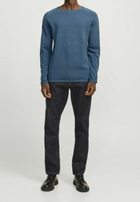 Blåstickad långärmad tröja med rund halsringning, kombinerad med mörka jeans och svarta skor. Tyget har en texturerad yta.